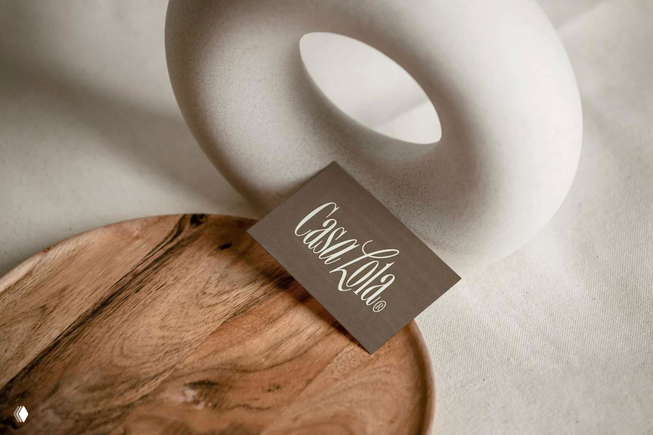 Визитная карточка Casa Lola рядом с керамическим декором и деревянной подложкой; логотип на тёплом коричневом карточном материале