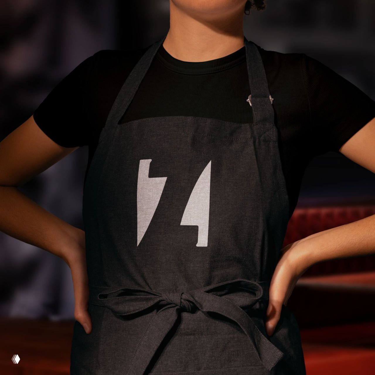 Фартук официантки с нанесённым белым знаком Zelman Meats на тёмном фоне: демонстрация логотипа в интерьере и фирменной одежде ресторана.