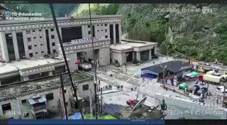Горный посёлок у ущелья: здания и дороги у реки, видны следы обвала и завалы на берегу после стихийного бедствия.