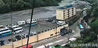 Река с мутной водой у набережной: повреждённые ограждения и стоянка автобусов рядом, видна разрушенная береговая зона.