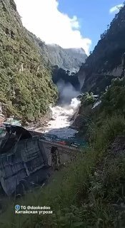 Бурный поток воды в ущелье у разрушенной плотины или сооружения, кадр показывает мощный напор и разрушения на берегу.
