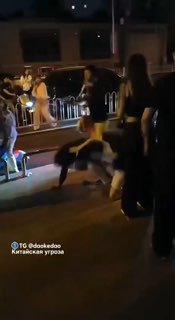 Ночная уличная сцена в Сюйчжоу: толпа удерживает иностранца на коленях после стычки, вокруг свидетели, металлические ограждения и тротуар.