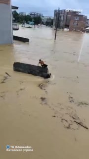 Человек на обломке в разлившейся реке в Гуанси: сильный поток мутной воды вокруг затопленных домов, сцена отражает масштаб подтопления и опасность для людей.
