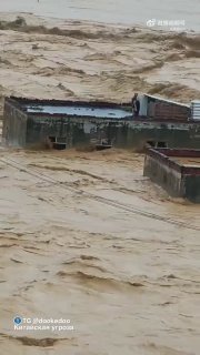 Затопленный жилой район в Гуанси: бурые потоки воды окружают дома, видны разрушения крыш и сильное движение наносов, вертикальный кадр.