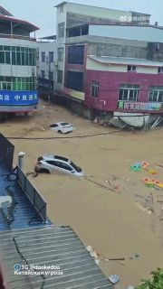 Улица в Гуанси, заполненная коричневой водой: автомобили частично погружены, поток несёт мусор и создает серьёзные препятствия, вертикальное видео с высоты.