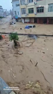 Широкий план затопленной улицы в Гуанси: мутная вода стремительно течёт, сносит ограждения и мешает движению, кадр вертикального видео с общего плана.