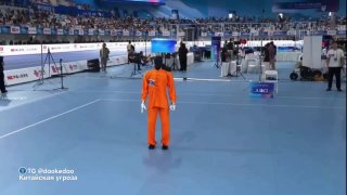 Человек в оранжевом костюме демонстрирует «пьяный» стиль робокунгфу на спортивной арене; видны судьи и трибуны.
