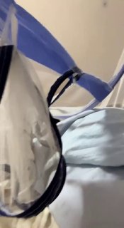 Медицинские маски и прозрачные лицевые щитки, подвешенные на крючках в помещении; крупный план защитных средств на размытом фоне.