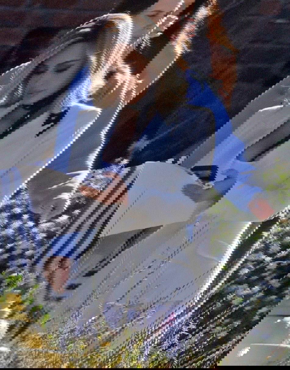 Персона в белом жакете с чёрным платком на шее просматривает сценарий и держит телефон на внешней локации съёмок фильма.