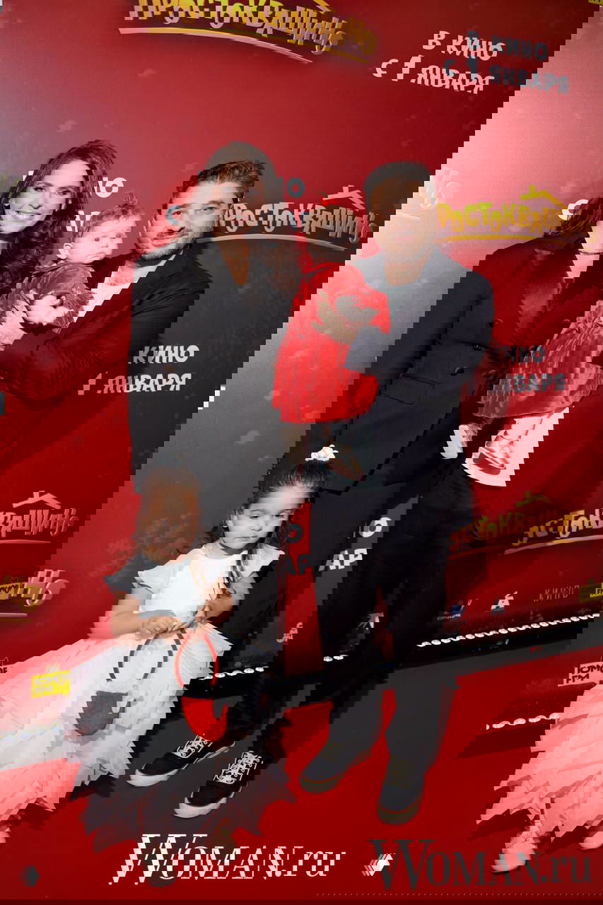 Семейный снимок на премьере: супруги с двумя дочками позируют на красной дорожке на фоне логотипа фильма и постера.