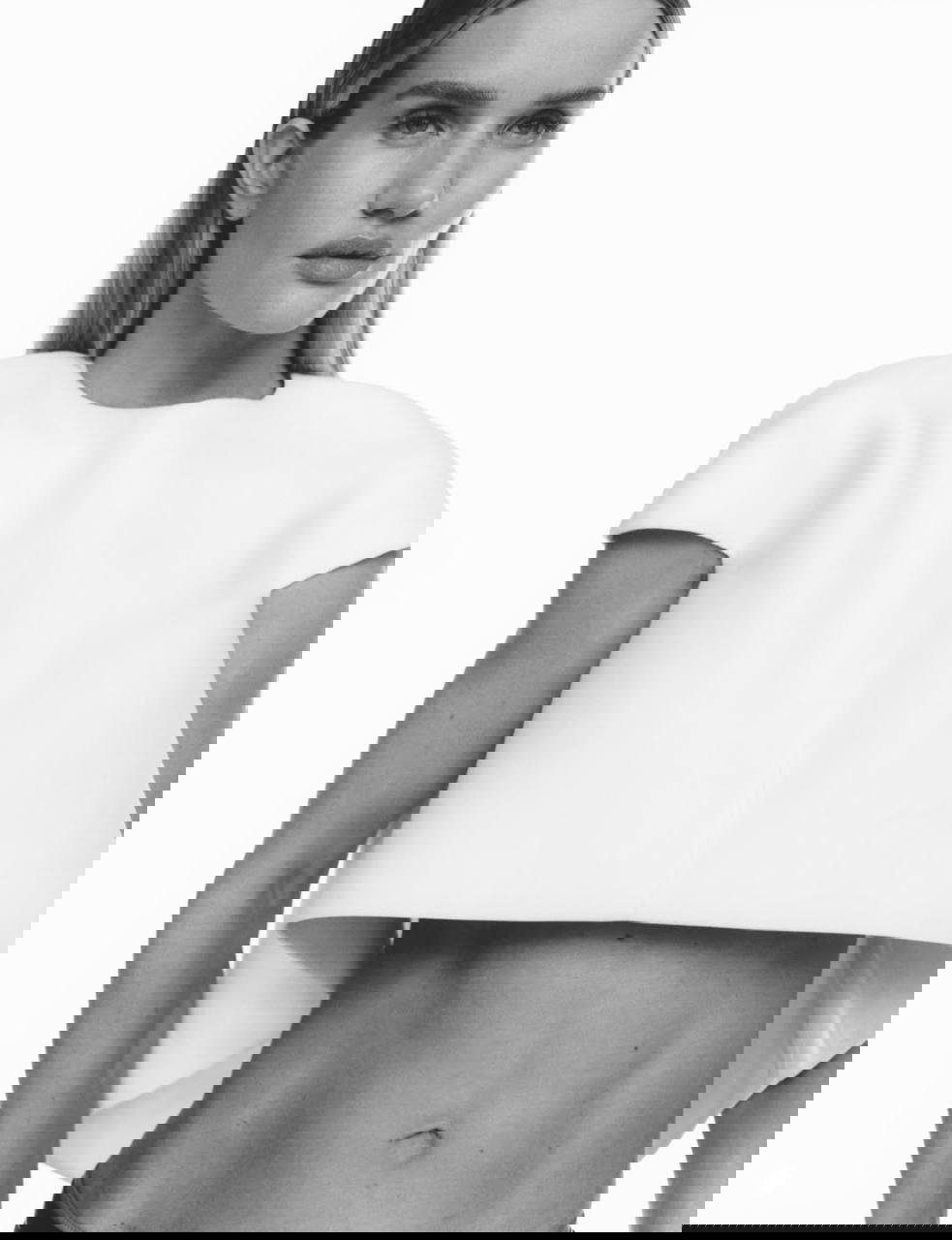 Частичный кадр в светлом кроптопе на белом фоне: минималистичная подача и акцент на линии талии и живота модели.