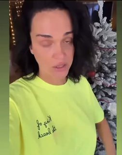 Вертикальный кадр из видео: певица Слава в салатовой футболке на фоне украшенной ёлки, выглядит расстроенной и обращается в камеру.