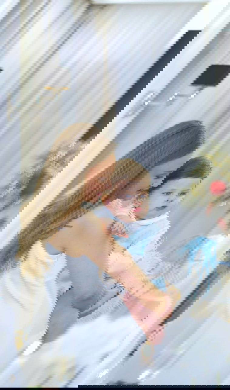 Женщина в светлом платье держит младенца на руках на торжестве; в кадре заметны праздничные детали интерьера и мягкое освещение, семейная фотография на мероприятии.