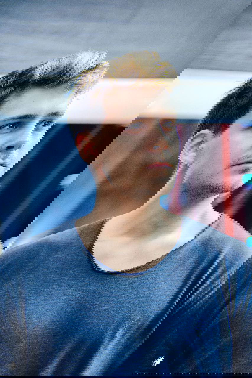 Портрет Милоша Биковича в повседневной футболке, крупный план лица, задумчивый взгляд и мягкое боке на заднем плане.