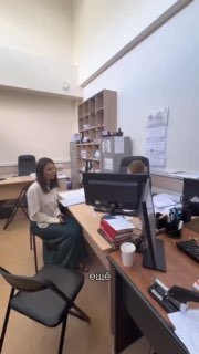 Кадр из видео: женщина сидит в кабинете у компьютерного стола, на столе папки и документы; сцена иллюстрирует обращение в правоохранительные органы.