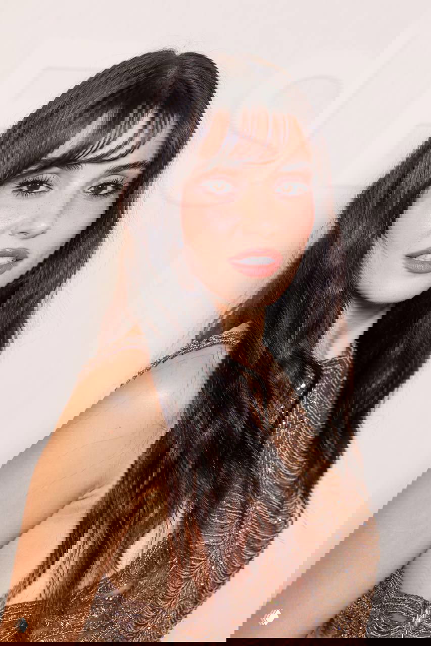 Крупный план лица Ханде Эрчел на показе Elie Saab в Москве: чёлка, натуральный макияж, текстура кожи и детализированный украшенный бисером топ на фоне светлой стены.