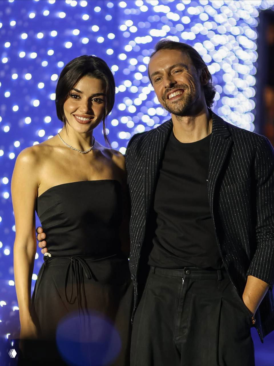 Ханде Эрчел и соратник по съёмочной группе улыбаются на фотоколле — вечерняя атмосфера и световые эффекты на фоне