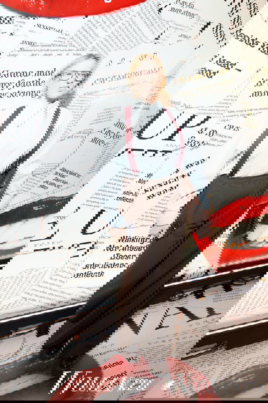 Женщина в рубашке и подтяжках позирует у фотозоны с газетными фрагментами, логотипом Zivert и крупными красными губами, оформлявшими стену