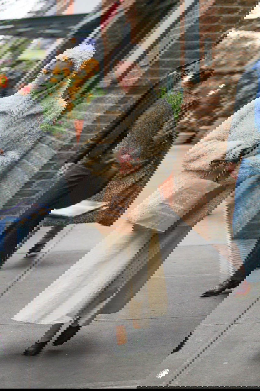 Фотография Ани Тейлор‑Джой в кремовом образе: длинная юбка и пушистая верхняя одежда на тротуаре города, сумка в руках.