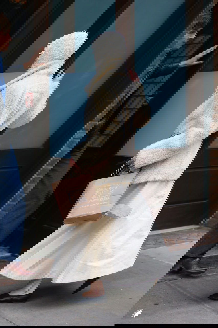 Аня Тейлор‑Джой снимается сзади в кремовой шубе и капюшоне, идёт в сторону входа в здание, папарацци фиксируют кадр.