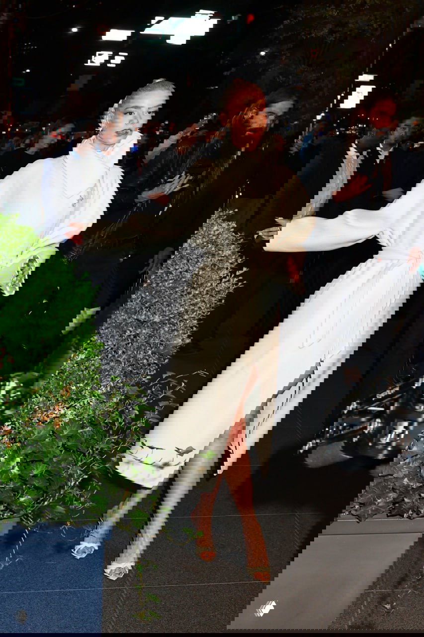 Аня в светлом ансамбле с бумажным пакетом в руке выходит из двери, белая юбка и текстура верхней одежды хорошо видны на улице.