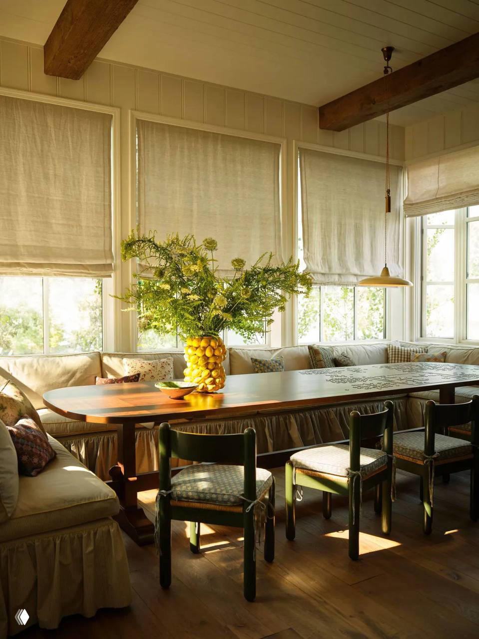 Светлая столовая с длинным деревянным столом, шторы из натуральных тканей и большой букет лимонов на вазе — натуральный и деревенский стиль интерьера.