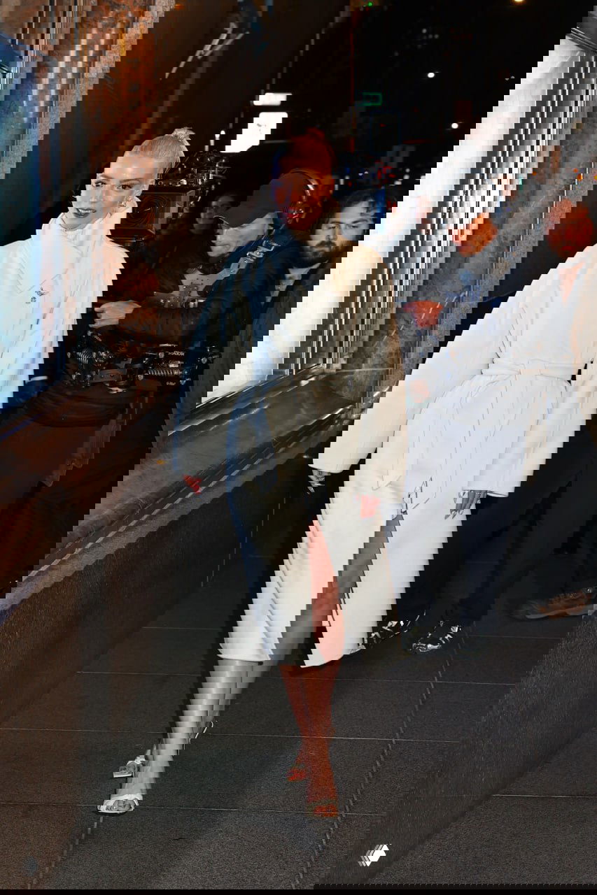 Крупный план: Аня Тейлор‑Джой в белом пальто с эффектным воротником и собранными волосами, папарацци и толпа на заднем плане.