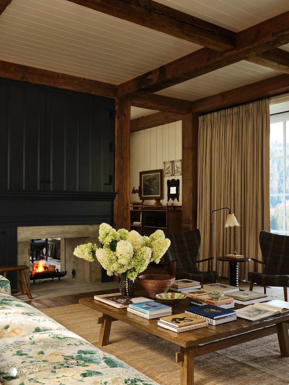 Интерьер с камином, низким деревянным столом и вазой с гортензиями на фоне деревянных балок и сдержанных текстур — уютные акценты дома в горах.