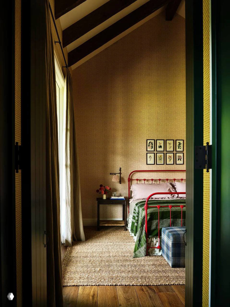 Узкая спальня с красной металлической кроватью, пледами и соломенным ковром: простые детали в стиле grandma‑chic и теплые деревянные полы горного дома.