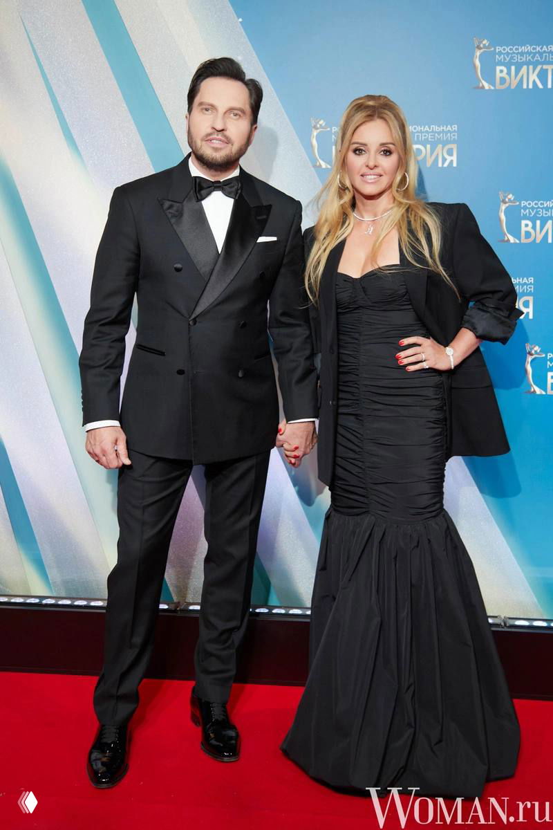 Александр Ревва с женой на красной дорожке премии «Виктория»: пара в вечерних образах позирует перед фотостеной с логотипом.