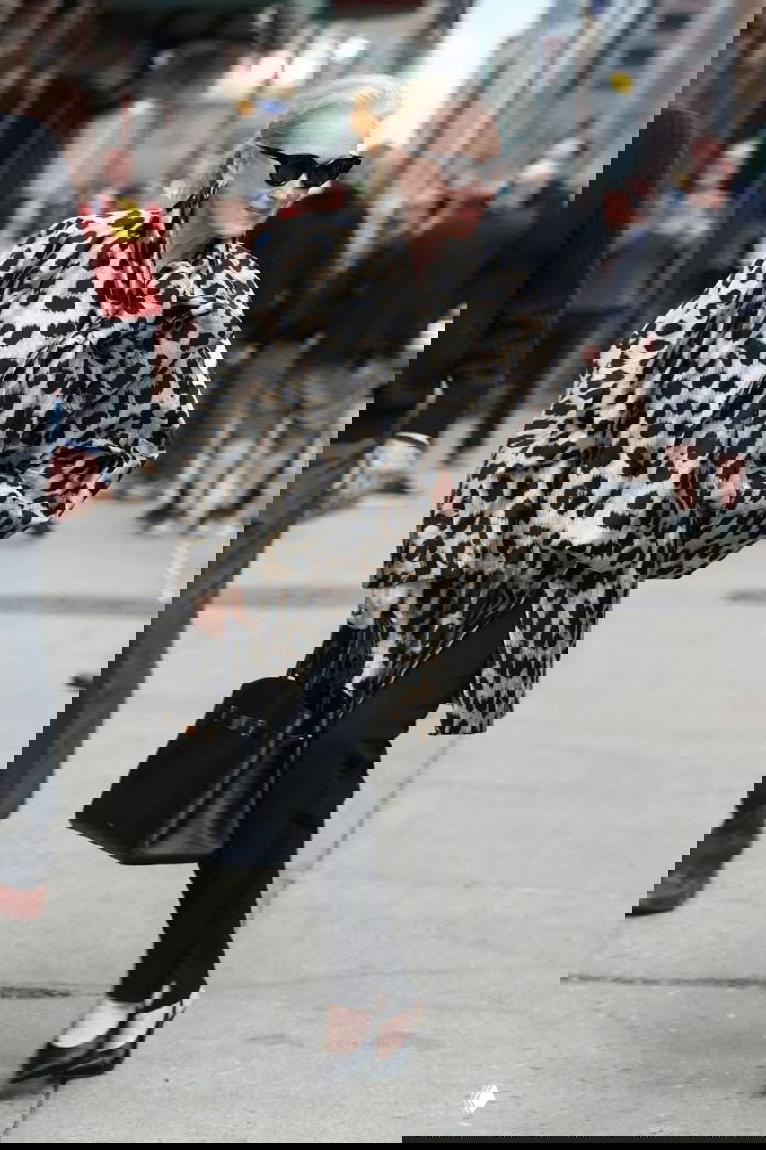 Крупный план: Мэрил Стрип в пальто с леопардовым принтом Givenchy, улыбается и держит чёрную сумку на фоне прохожих в Нью-Йорке.