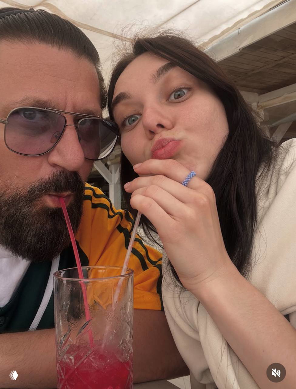 Фото Виктора и Марии в летнем кафе: они делят напиток через соломинки, Мария позирует близко к камере в непринуждённой манере.