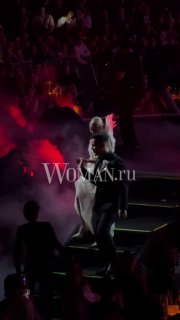 Клава Кока и Дима Масленников идут по проходу в нарядах, похожих на свадебные, пара целуется на публике при тусклой подсветке арены.