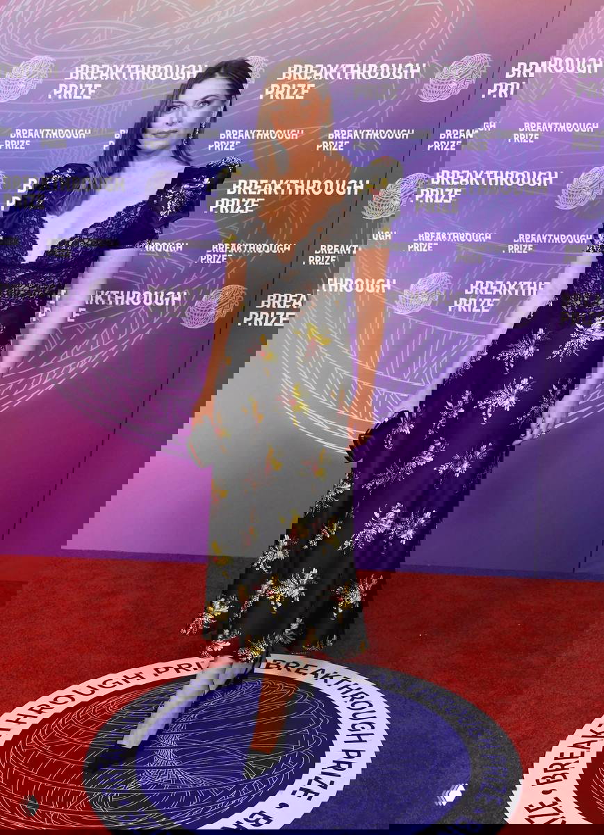 Женщина в черном платье с кружевным корсетом и цветочным принтом стоит на красной дорожке Breakthrough Prize 2026.