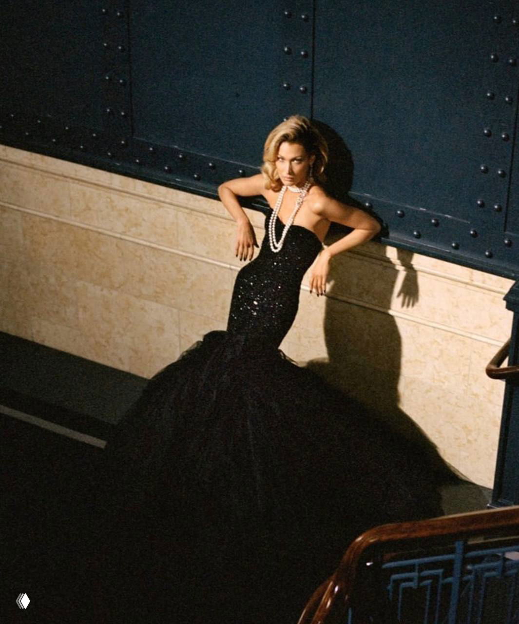 Модель в чёрном вечернем платье-русалке, драматичный свет и длинный подол; кадр с архитектурными тенями и элегантной позой.
