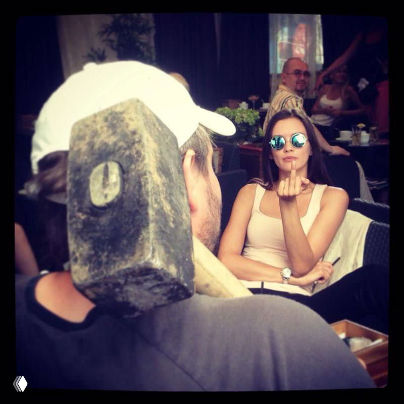 Кадр с натуры: актриса в солнечных очках в кафе, рядом рабочие и реквизит — повседневный закулисный снимок со съёмочной паузы.