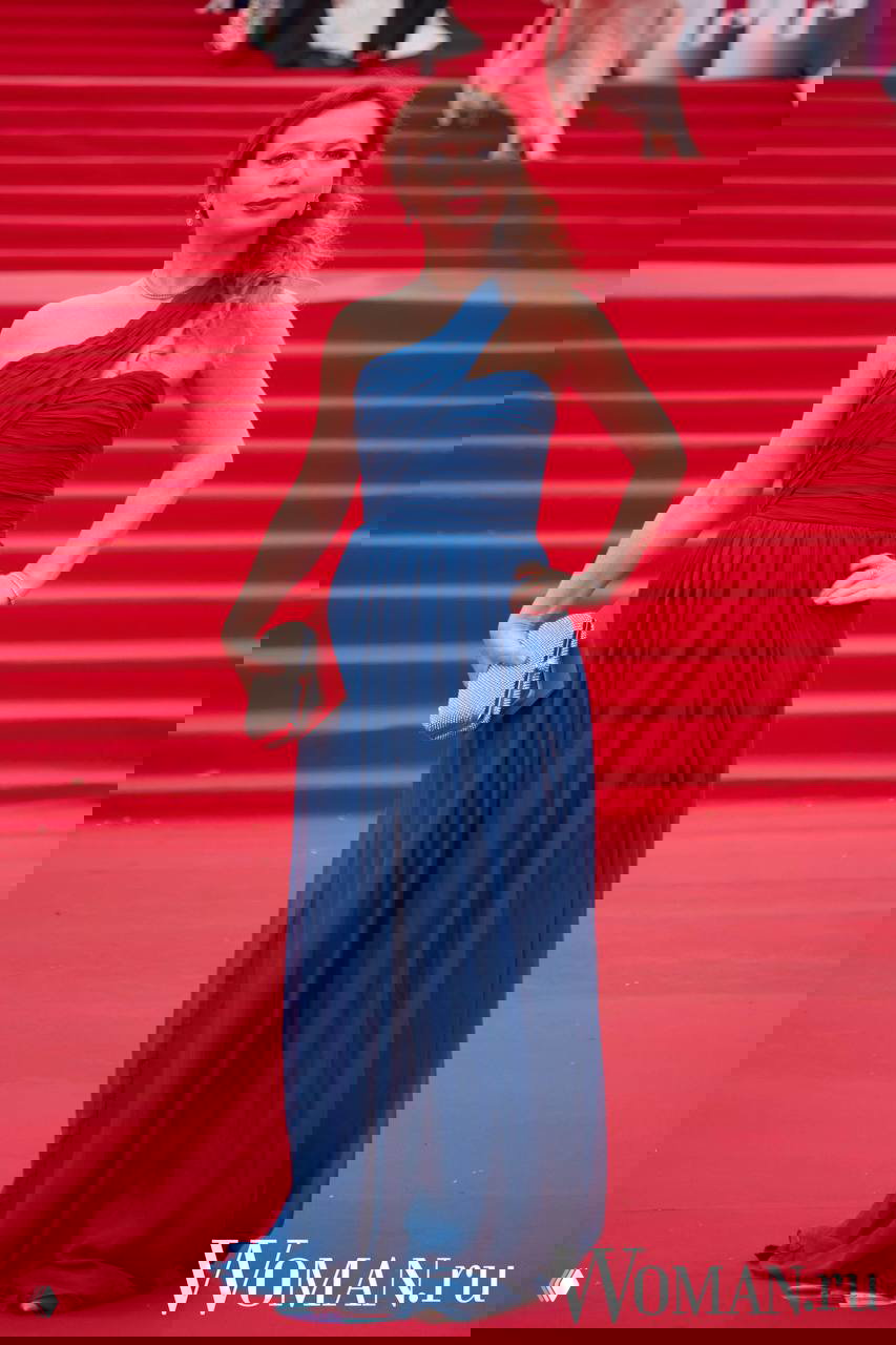 Женщина в асимметричном синем вечернем платье с клатчем позирует на красной дорожке 48-го Московского ММКФ, демонстрируя силуэт в полный рост.