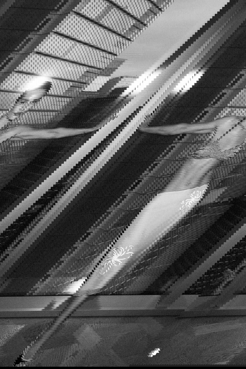 Чёрно‑белая фотография Роузи в бра и юбке на фоне стеклянных высотных зданий — городская глянцевая съёмка.