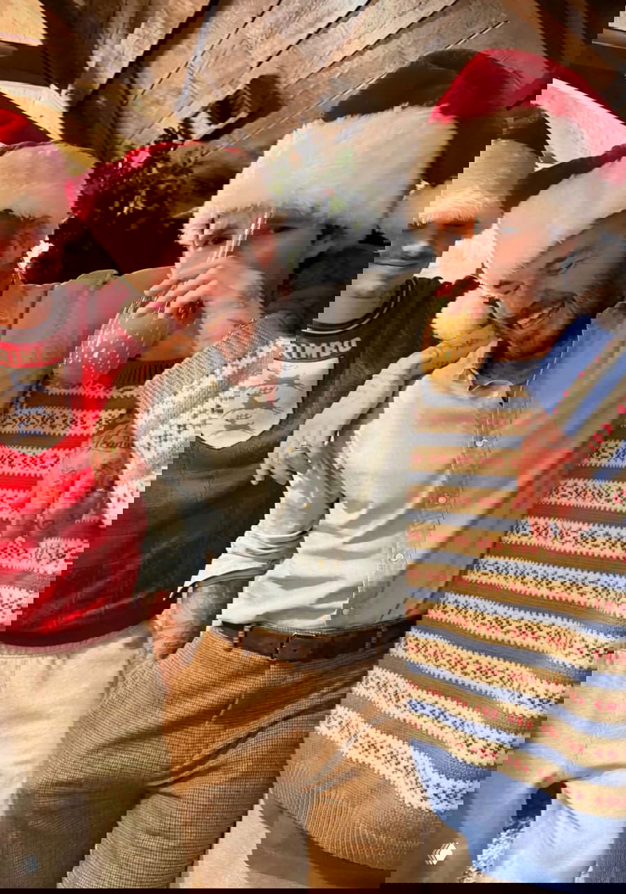 Трое людей в шапках Санты стоят плечом к плечу; один пьёт напиток через трубочку — дружеская и непринуждённая праздничная сцена.