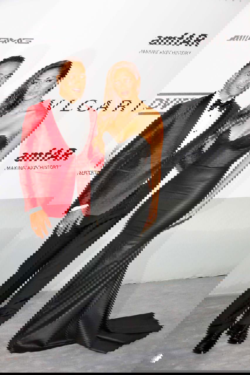 Мужчина в смокинге и женщина в обтягивающем черном платье позируют на благотворительном вечере на фоне логотипов спонсоров, формальный кадр.