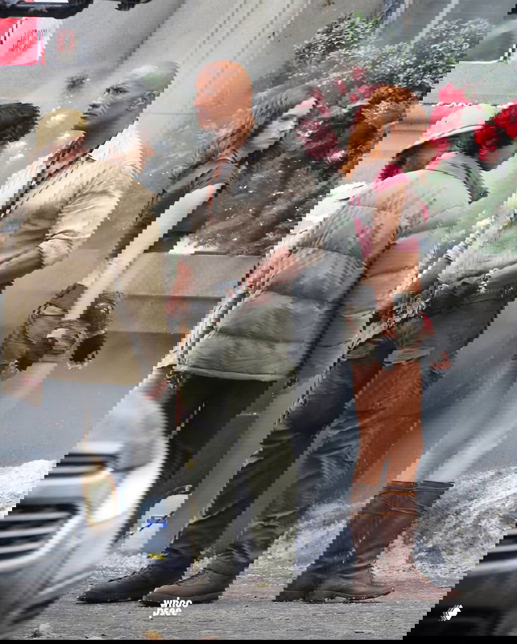 Группа актёров в костюмах на городском фоне: мужчина в грубой рубашке и женщина в коротких шортах, вокруг съёмочная техника и декорации.