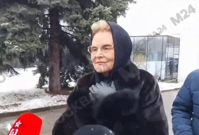 Елена Малышева в чёрном платке и шубе дает комментарий журналистам на фоне заснеженной аллеи у Троекуровского кладбища во время прощания.