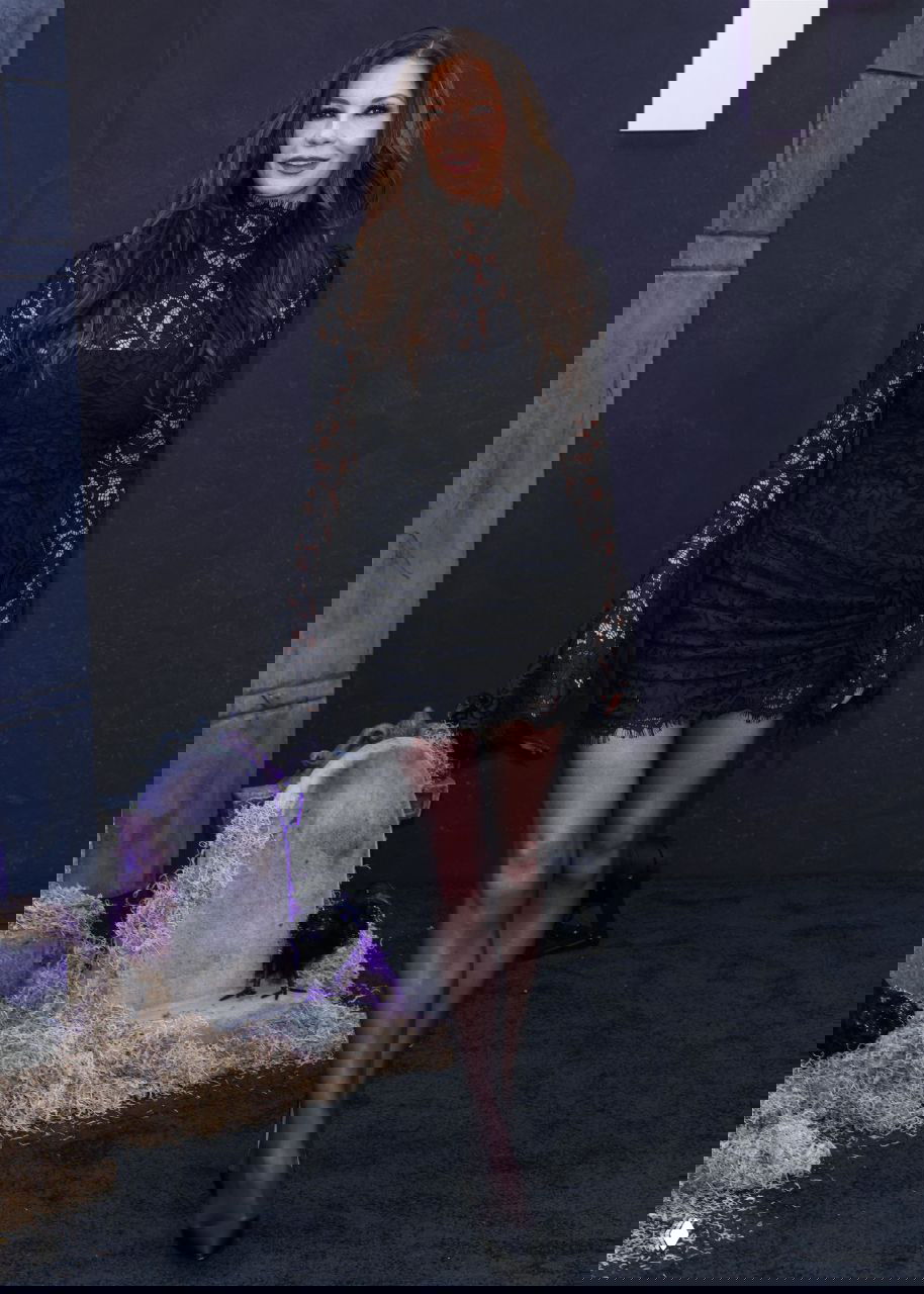 Кэтрин Зета‑Джонс в чёрном кружевном мини‑платье позирует на фоне сценографии с надгробиями и декоративными воронами на мероприятии.