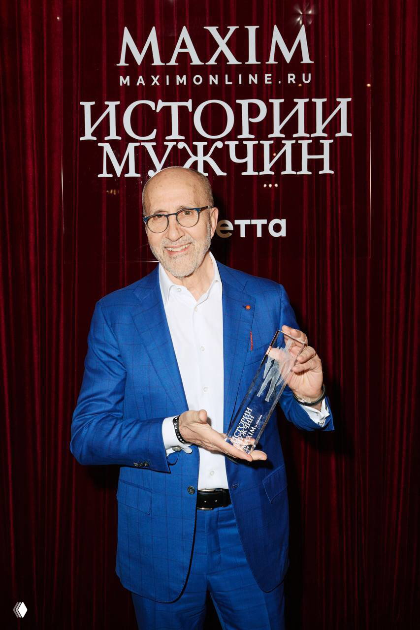 Награждаемый в синем костюме улыбается и держит прозрачную статуэтку на фоне красной занавески с логотипом Maximonline и надписью
