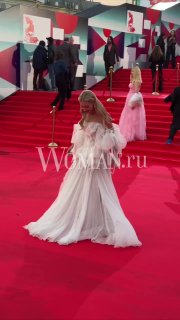 Кристина Асмус в белом многослойном платье на красной дорожке ММКФ; в кадре видно движение платья и гостей фестиваля.