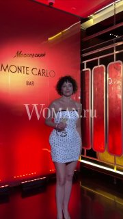 Екатерина Волкова в белом гороховом платье с бокалом на фоне неоновой сцены Monte Carlo Bar; кадр с логотипом Woman.ru