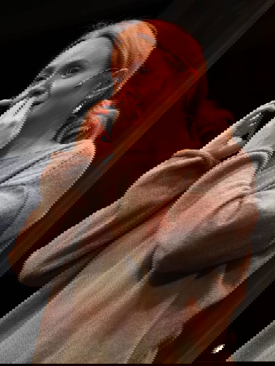 Актриса на сцене в крупном плане: телефон у уха, рука у рта, слёзы на глазах — эмоциональный театральный момент