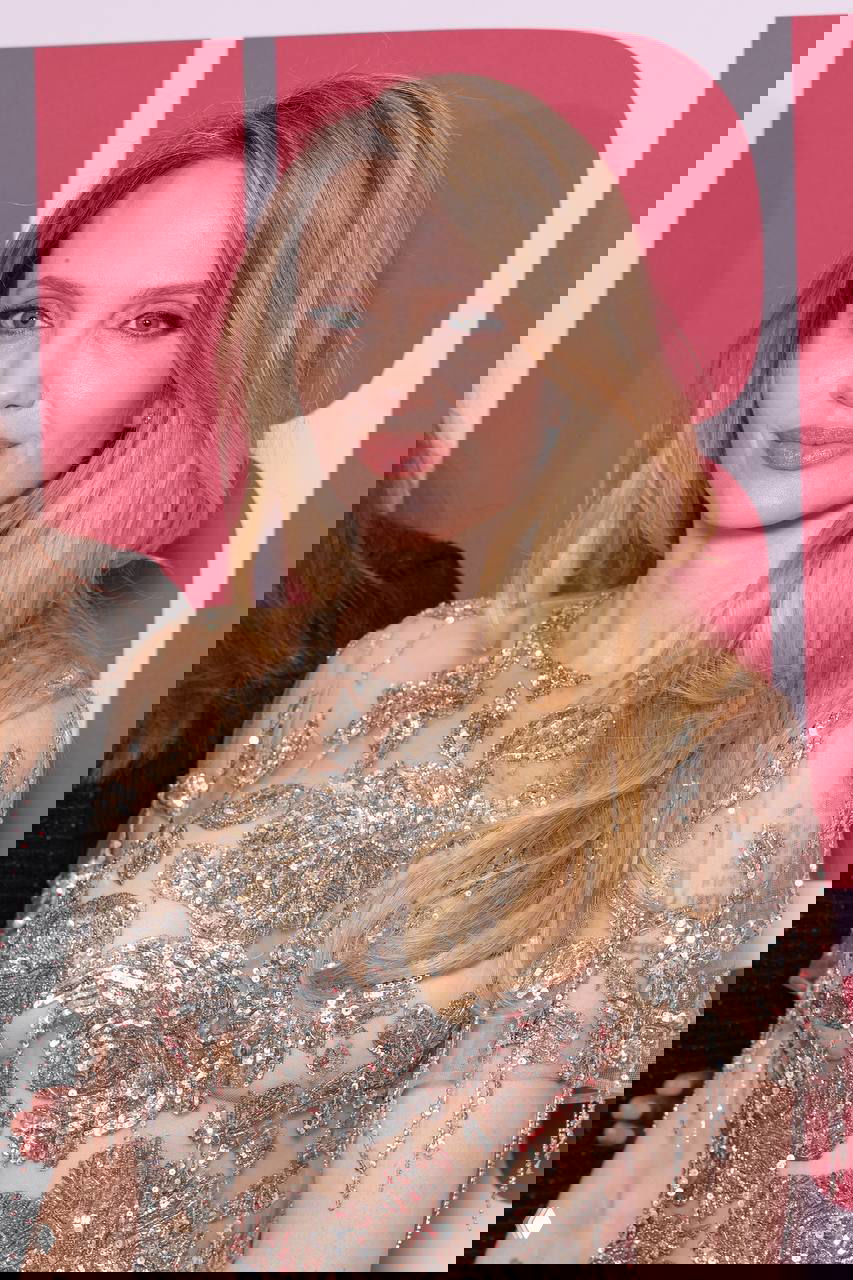 Крупный план женщины в украшенном серебристой вышивкой платье: аккуратный макияж и распущенные светлые волосы на фотоколле премьеры.