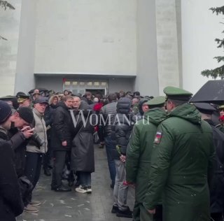 Очередь посетителей и присутствие людей в тёплой одежде рядом с охраной и венками у входа на Троекуровское кладбище во время похорон журналиста.