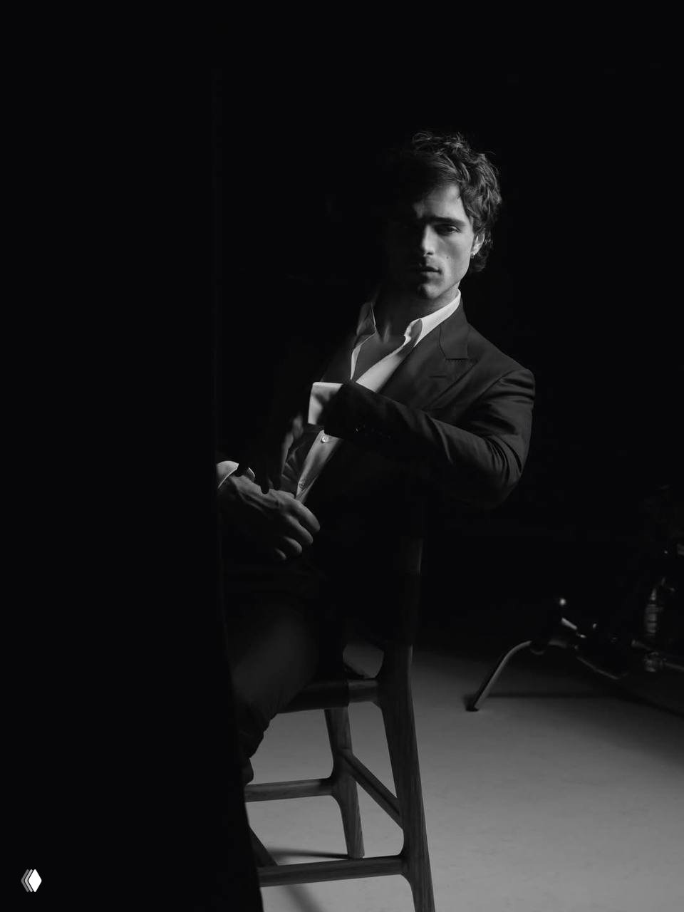 Репродукция чёрно‑белого кадра: мужчина в костюме сидит на стуле в полумраке студии, художественная съёмка для рекламы.